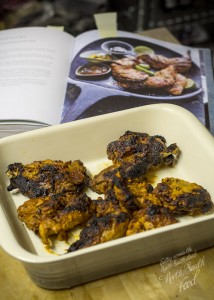 Grilled tandoori pheasant pieces in shallow dish, beside book